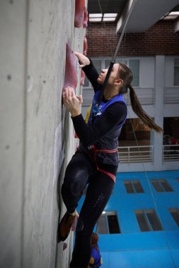 Güçlü genç bayan tırmanıcı, kapalı alanda tırmanma yarışmasında hız duvarına tırmanır. Kyiv - 6 Mart 2024