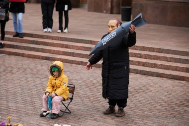 2022 yılında Mariupol Tiyatrosu 'na yapılan Rus saldırısının yıldönümü anısına düzenlenen sanat gösterisi sırasında Putin maskeli aktör Ukraynalı çocuğu hedef almıştı. Kyiv - 17 Mart 2024