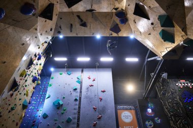 Spor salonundaki yüksek tırmanma duvarında güvenlik halatına asılı duran bir tırmanıcı. Kyiv - 10 Mart 2024