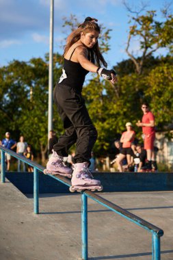 Roller girl grinding on a handrail in skate park. Frontside grind trick. Kyiv - 4 August,2024 clipart