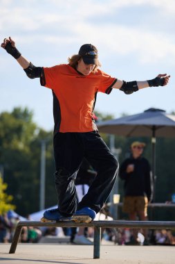 Teen roller blader performing sweat stance trick on a rail in skatepark. Kyiv - 4 August,2024 clipart