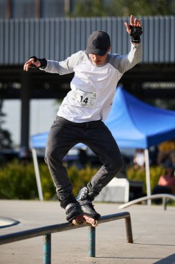 In-line skater grinding on a rail. Roller blader performing mistrial trick in a skatepark. Kyiv - 4 August,2024 clipart