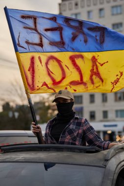 Young Ukrainian nationalist rides in a car with blue and yellow flag of Ukraine in hands and writing Free Azov. Kyiv - 15 September,2024 clipart