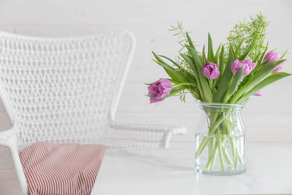 Wicker white chair and a bouquet of tulips on the table, relaxation corner