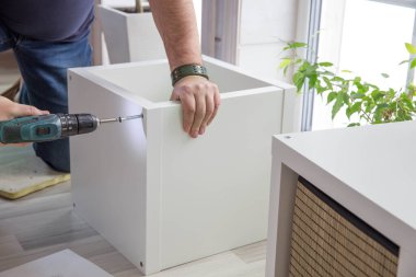 Bir adam büyük pencereli güzel bir odada mobilya monte etti. DIY veya mobilya montaj hizmetleri kavramı