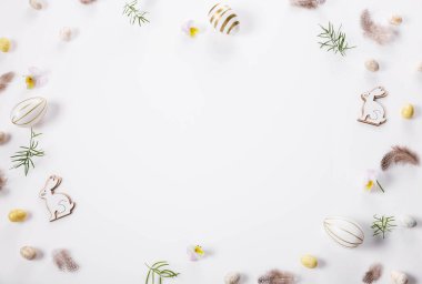 Flat lay of Easter decor on white background, featuring wooden bunnies, decorative Easter eggs, feathers, and greenery. Minimalist Easter frame with free space for text, seasonal designs or invitation clipart