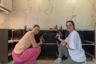 DIY mutfak toplantısı sırasında gülümseyen iki kadın, kablosuz matkaplar, mermer duvarlı modern iç mekan, ev geliştirme, takım çalışması konsepti, kadın inşaatçılar, gerçek yenileme anı