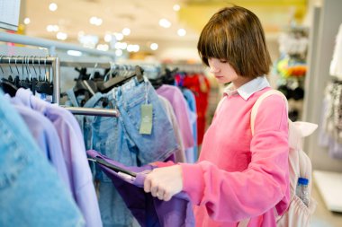 Güzel genç kız alışveriş merkezinde yeni kıyafetler seçiyor. Mağazada yeni kıyafet seçen bir genç. Satış, alışveriş ve moda konsepti.