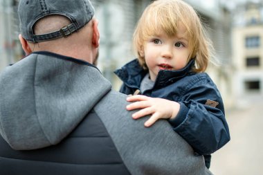 Babasının kollarında tatlı bir çocuk var. Baba ve oğul güneşli bir sonbahar gününde eğleniyorlar. Babası tarafından tutulan sevimli bir oğul. Sonbahar mevsiminde aktif aile zamanı.