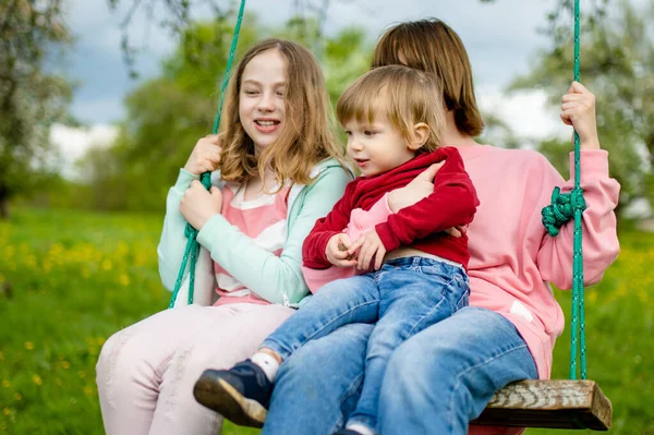 2人の妹とその弟は 暖かい春の日にリンゴ園の開花でスイングを楽しんでいます 子供連れの家族のための積極的な屋外活動 — ストック写真