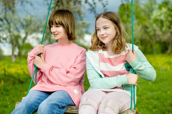 春暖花开的苹果园里 两个妹妹在荡秋千上玩得很开心 为有子女的家庭开展积极的户外活动 — 图库照片