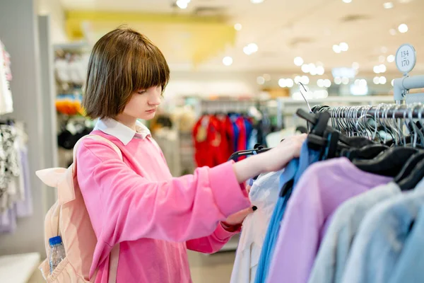 stock image Pretty teenage girl choosing new clothes in a shopping center. Teenager picking new clothing in a store. Sale, shopping and fashion concept.