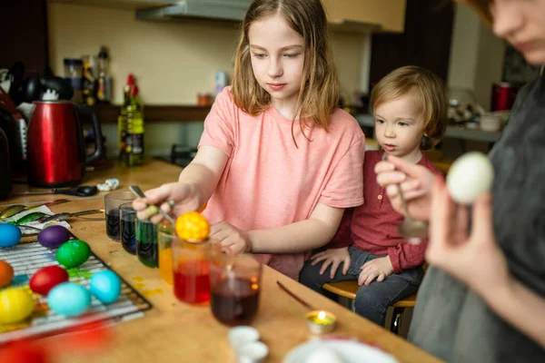 2人の姉と弟がイースターエッグを自宅で染色している 子供たちはイースターハントのためにカラフルな卵を描く 子供たちはイースターのお祝いの準備を 家族の伝統 — ストック写真