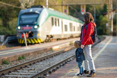 Genç anne ve küçük oğlu bir tren istasyonunda. Anne ve küçük çocuk platformda tren bekliyor. Aile seyahate hazır. Küçük çocuklarla tatile gidiyorum..