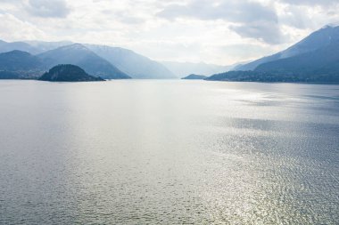 Güneşli yaz gününde ünlü Como Gölü 'nün güzel hava manzarası. Gölün sakin sularına yansıyan bulutlar ve arka planda Alp dağları. Lombardy, İtalya.