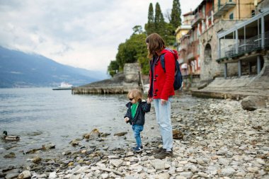 Annesi ve küçük oğlu, Como Gölü kıyısındaki en pitoresk kasabalardan biri olan Varenna 'da ördek besliyor. Tipik İtalyan atmosferiyle büyüleyici bir yer. Varenna, Lombardy, İtalya.