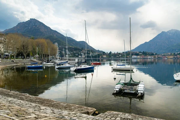 Colourful yachts docked at marina of Lecco town on spring day. Picturesque waterfront of Lecco located between famous Lake Como and scenic Bergamo Alps mountains. Vacation destination in Italy.