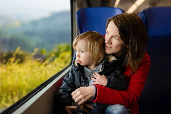 年轻的母亲和她蹒跚学步的儿子乘火车旅行 全家度假时 妈妈和小孩坐在窗边的特快列车上 在火车车厢里的家人和小孩一起去度假 — 图库照片