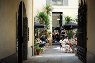 MILAN, ITALY - Mayıs 2011: İtalya 'nın kuzey Lombardiya bölgesinde yer alan bir metropol olan Milano' nun merkezindeki işlek caddenin dışındaki açık kafede oturan turistler ve yerel halk. Milan, Lombardiya, İtalya.