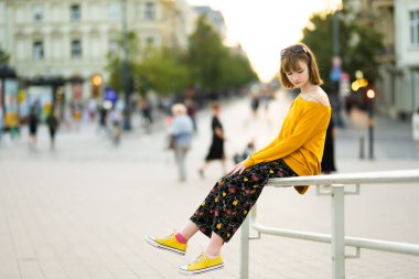 Sıcak ve güneşli bir yaz gününde Vilnius, Litvanya 'da gezen sarı kazak giyen sevimli genç kız. Çocuklarla aile eğlencesi..