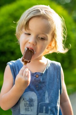 Sıcak, güneşli bir yaz gününde dışarıda tatlı taze dondurma yiyen tatlı çocuk. Çocuklar şeker yiyor. Çocuklar için sağlıksız yiyecekler.