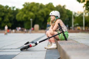 Güneşli bir yaz akşamında güzel bir genç kız mobiletiyle şehirde geziyor. Patenle gezen güzel bir çocuk. Çocuklar için aktif eğlence ve açık hava sporları.