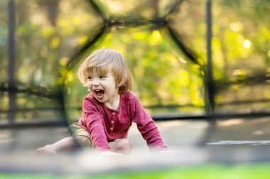 Sıcak ve güneşli bir yaz gününde arka bahçede trambolinde zıplayan tatlı çocuk. Çocuklar için spor ve egzersiz. Yazın açık hava eğlence aktiviteleri.