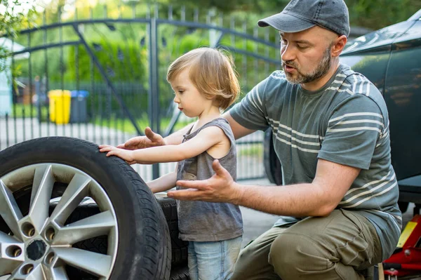 かわいい幼児の少年は 父親が裏庭で車の車輪を変えるのを助けています 父は息子に道具の使い方を教える 小さな子供のアクティブな親 — ストック写真