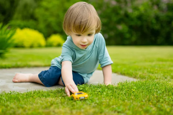 黄色のおもちゃの車で屋外で遊んでかわいい幼児の男の子 子供は自然を探検する おもちゃで楽しんでいる小さな子供 小さな子供のための夏の活動 — ストック写真