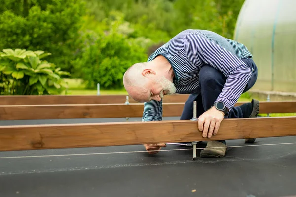 老年人在自家花园里的一个项目上工作 人类在后院建造了一个木制平台 — 图库照片
