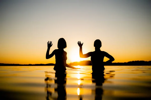 暖かく晴れた夏の夜に湖で楽しんでいる10代の女の子のシルエット 日没の若い女の子 家族の夏の活動 — ストック写真