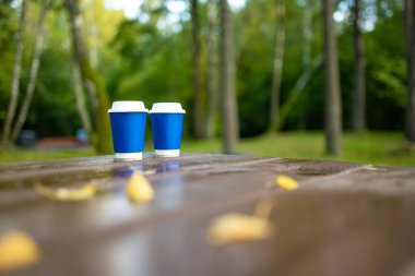 Açık kafedeki ahşap masada iki kağıt kahve fincanı. Yağmurlu bir sonbahar gününde doğayı keşfetmek. Sonbaharda etkinlik ve eğlence.