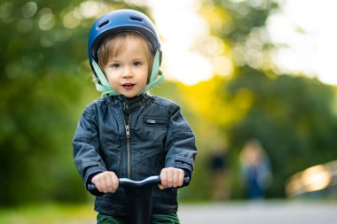 Sonbahar günü dışarıda bebek scooter 'ı süren komik çocuk. Şehir parkında bisiklete binen çocuk dengesi. Doğayı keşfeden çocuk. Küçük çocuklar için sonbahar aktiviteleri.