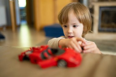 Kırmızı oyuncak arabayla oynayan tatlı bir çocuk. Küçük çocuk oyuncaklarla eğleniyor. Çocuk evdeki sıcak bir oturma odasında vakit geçiriyor. Evde aile eğlencesi..