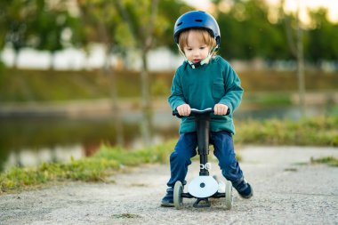 Sonbahar günü dışarıda bebek scooter 'ı süren komik çocuk. Şehir parkında bisiklete binen çocuk dengesi. Doğayı keşfeden çocuk. Küçük çocuklar için sonbahar aktiviteleri.