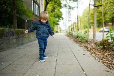 Komik çocuk güneşli bir sonbahar gününde dışarıda eğleniyor. Doğayı keşfeden çocuk. Şehir parkında yürüyen bir çocuk. Küçük çocuklar için sonbahar aktiviteleri.