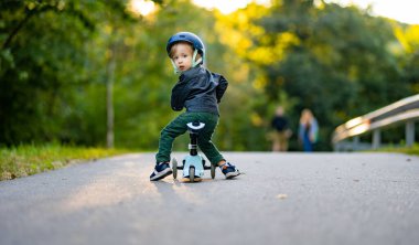 Sonbahar günü dışarıda bebek scooter 'ı süren komik çocuk. Şehir parkında bisiklete binen çocuk dengesi. Doğayı keşfeden çocuk. Küçük çocuklar için sonbahar aktiviteleri.