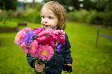 Elinde renkli paskalya çiçekleri tutan tatlı çocuk. Sonbahar günü bahçede taze çiçek toplayan bir çocuk. Annesi için çiçek seçen bir çocuk..
