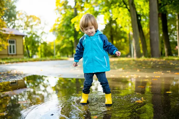 一个可爱的小孩穿着黄色的橡胶靴 在一个阳光灿烂的秋日在城市公园的水坑里玩耍 儿童探索自然 小孩儿们的秋季娱乐活动 — 图库照片