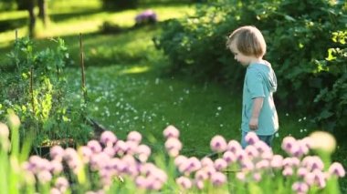 Cute toddler boy watering flower beds in the garden at summer day. Child using garden hose to water vegetables. Kid helping with everyday chores. Mommys little helper.