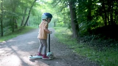 Yazın dışarıda bebek scooter 'ı süren komik çocuk. Şehir parkında bisiklete binen çocuk dengesi. Doğayı keşfeden çocuk. Küçük çocuklar için açık hava aktiviteleri. Yavaş çekim görüntüleri,