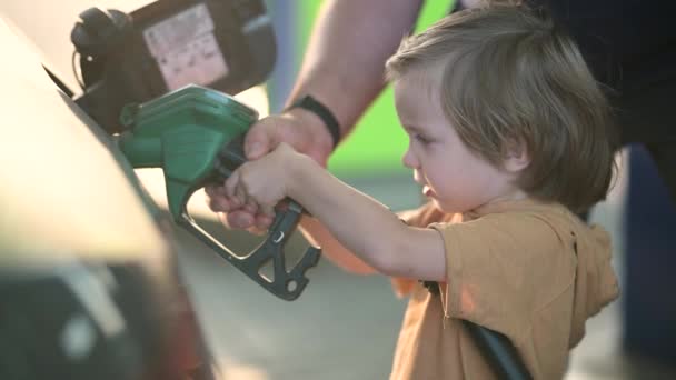 かわいい金髪の少年がポンプノズルを握り 父親がガソリンスタンドで車を燃やすのを手伝った 小さな子供のヘルパー クローズアップスローモーション映像 — ストック動画