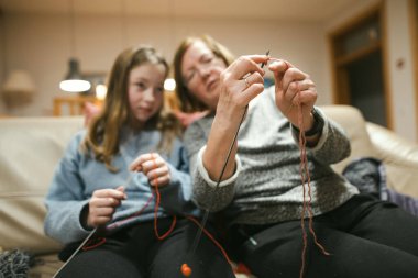 Büyükanne ve genç torun kanepede örgü örüyor. Büyükannem ergen çocuklara örgü örmeyi öğretiyor. Ebeveynler ve çocuklar için el işleri ve hobiler.