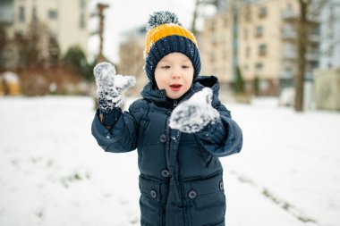 Tatlı çocuk, karlı bir kış gününde şehirde eğleniyor. Karda oynayan, kalın giysiler giymiş şirin bir çocuk. Çocuklu aileler için kış etkinlikleri.