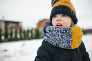 Tatlı çocuk, kar yağışlı kış gününde arka bahçede eğleniyor. Karda oynayan, kalın giysiler giymiş şirin bir çocuk. Çocuklu aileler için kış etkinlikleri.