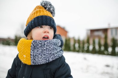 Tatlı çocuk, kar yağışlı kış gününde arka bahçede eğleniyor. Karda oynayan, kalın giysiler giymiş şirin bir çocuk. Çocuklu aileler için kış etkinlikleri.