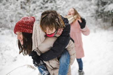 Komik genç kız kardeşler ve anneleri serin kış günlerinde karla kaplı çam ormanlarında yürüyüş yaparken eğleniyorlar. Doğayı keşfeden genç kızlar. Çocuklar için kış aktiviteleri.