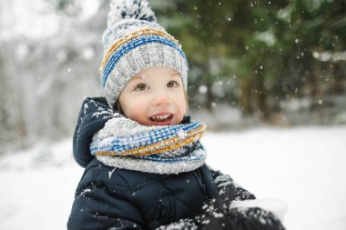 Tatlı çocuk serin kış günlerinde karla kaplı bir çam ormanında yürüyüş yaparken eğleniyor. Doğayı keşfeden çocuk. Küçük çocuklar için kış aktiviteleri.