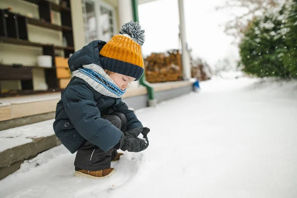 雪の冬の日に裏庭で楽しんでいる愛らしい幼児の少年 雪の中で遊ぶ暖かい服を着てかわいい子供 子供連れの家族のための冬の活動 — ストック写真