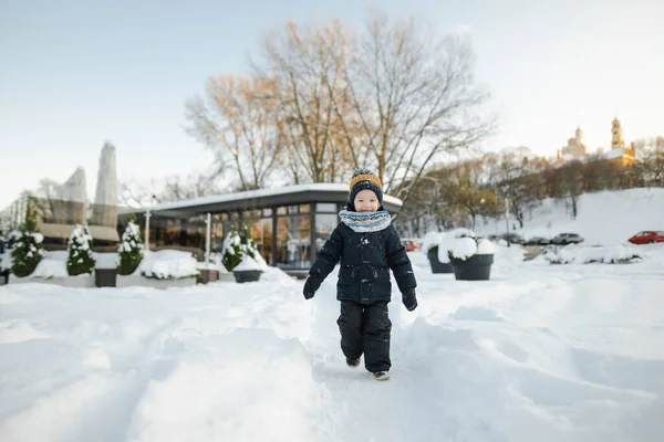 雪の降る冬の日に街で楽しんでいる愛らしい幼児の少年 雪の中で遊ぶ暖かい服を着ているかわいい子供 子供と家族のための冬の活動 — ストック写真